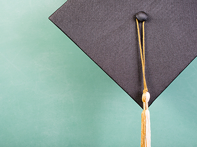 Closeup of grad mortarboard with gold and white tassel on green chalkboard background