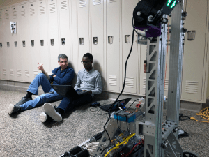 Male mentor sitting on floor with student with robot in foreground