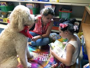 Young girl reading to attentive white poodle and owner