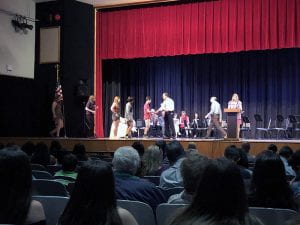 Line of students on stage receiving certificates from counselor