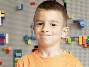 Smiling boy in orange shirt with Lego wall background