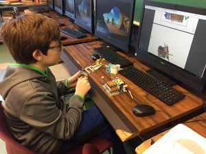 Student building LEGO robot components, looking at computer screen