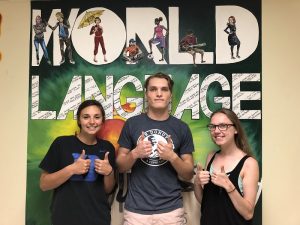 Three students giving thumbs-up in front of World Language mural